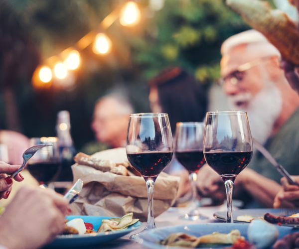 Happy family eating and drinking red wine at dinner barbecue party outdoor - Mature and young people dining together on rooftop - Youth and elderly weekend lifestyle activities - Focus on wineglass